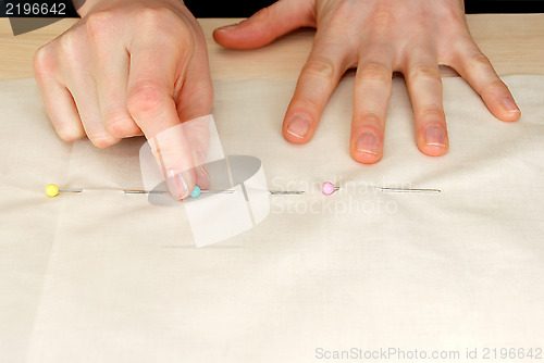 Image of Closeup of large upholstery pins being pinned into plain fabric