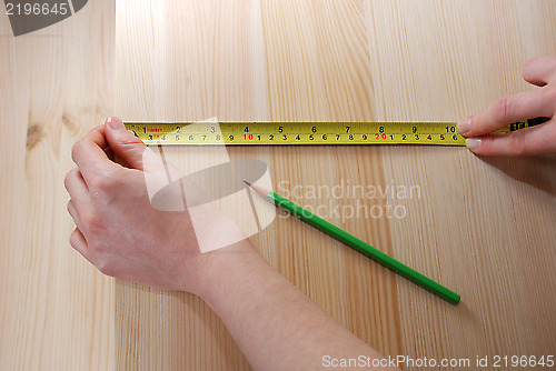 Image of Two hands measure a wooden board with a steel tape measure