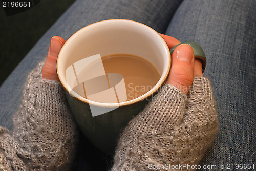 Image of A woman in a cosy jumper holds a cup of tea or coffee on her lap