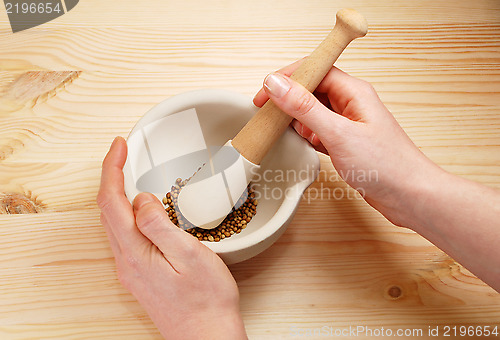 Image of Two hands holding a pestle and mortar with whole coriander seeds