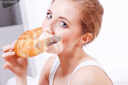Image of attractive young woman eating croissant