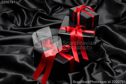 Image of Black gift boxe with red satin ribbons and bows, over black satin