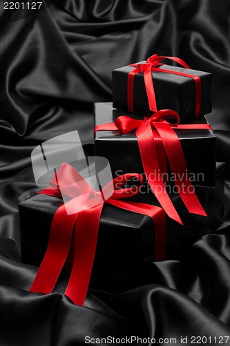 Image of Black gift boxe with red satin ribbons and bows, over black satin