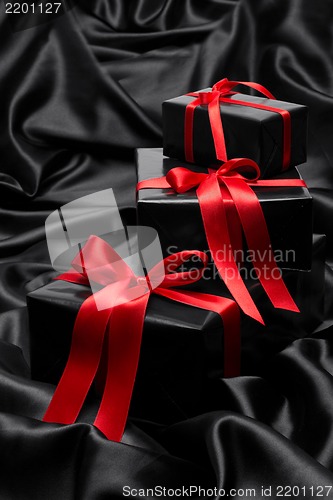 Image of Black gift boxe with red satin ribbons and bows, over black satin