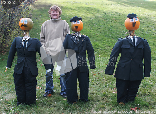 Image of Man poses with pumpkin people in suits