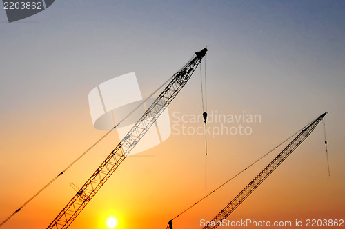 Image of Industrial construction cranes and building silhouettes over sun