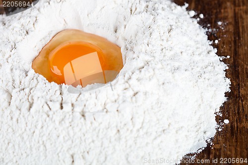 Image of broken egg on flour on wooden table