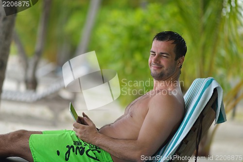 Image of man ralaxing and use tablet at beach