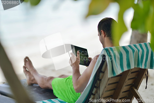 Image of man ralaxing and use tablet at beach