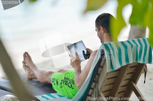 Image of man ralaxing and use tablet at beach