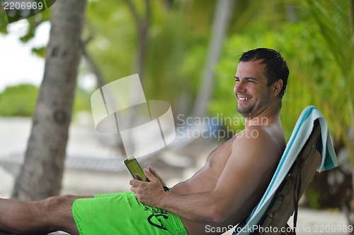 Image of man ralaxing and use tablet at beach