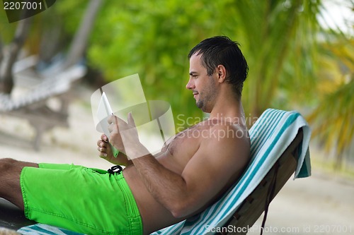 Image of man ralaxing and use tablet at beach