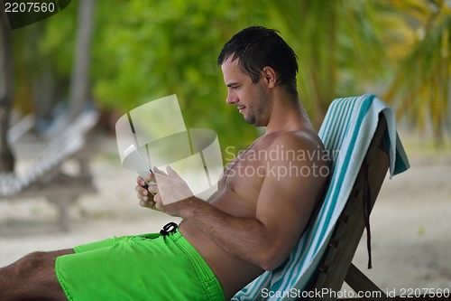 Image of man ralaxing and use tablet at beach