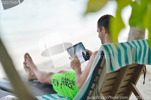 Image of man ralaxing and use tablet at beach