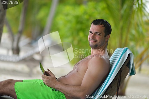 Image of man ralaxing and use tablet at beach