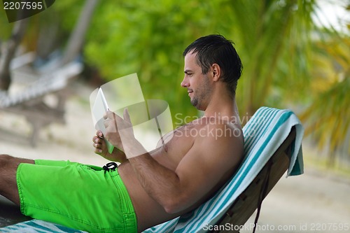 Image of man ralaxing and use tablet at beach