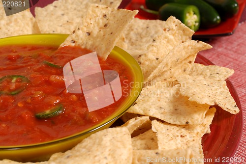 Image of A closeup of a bowl of salsa with tortilla chips and jalapeno pe
