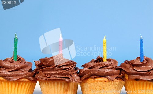 Image of Four chocolate frosted cupcakes in a row with candles