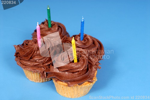 Image of Four chocolate frosted cupcakes with candles with a blue backgro