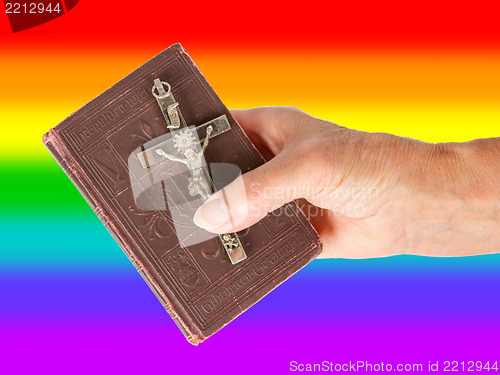 Image of Old hand (woman) holding a very old bible, rainbow flag