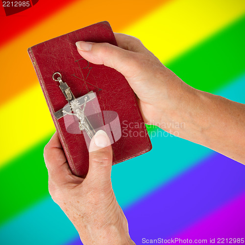 Image of Old hands holding a very old bible, rainbow flag pattern