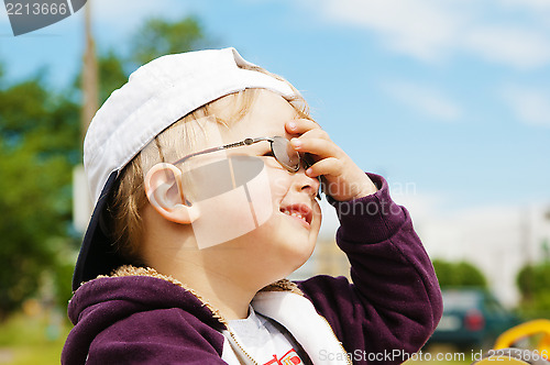 Image of Little boy in glasses hand covers the eyes from bright sun 