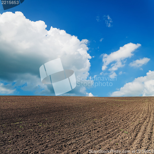 Image of black ploughed field under blue sky with clouds