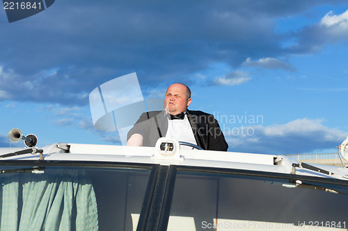 Image of Overweight man in a tuxedo at the helm of a pleasure boat