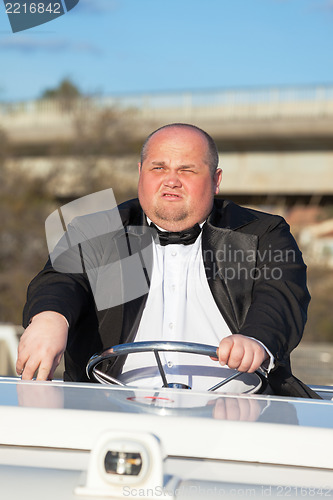 Image of Overweight man in a tuxedo at the helm of a pleasure boat