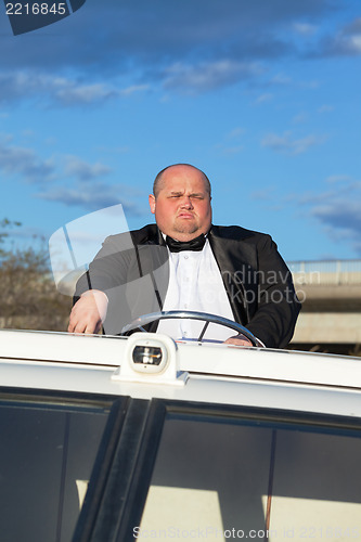 Image of Overweight man in a tuxedo at the helm of a pleasure boat