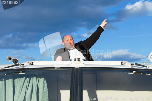 Image of Overweight man in a tuxedo at the helm of a pleasure boat