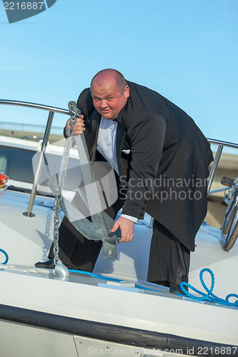 Image of Fat man in tuxedo lifting an anchor