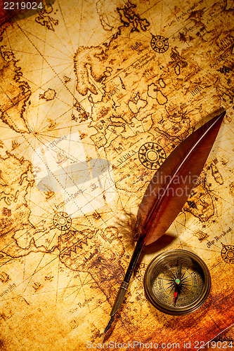 Image of Vintage compass and goose quill pen lying on an old map.