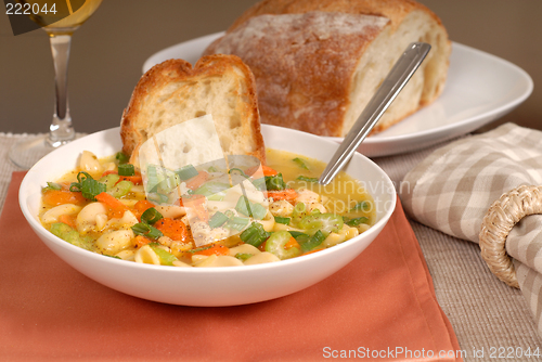 Image of A bowl of chicken noodle soup with rustic bread and a glass of w
