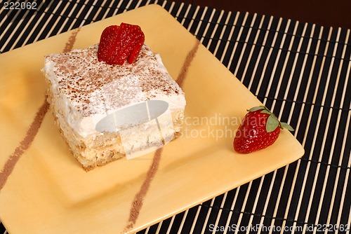 Image of A piece of tiramisu dusted with cocoa on a yellow plate with two