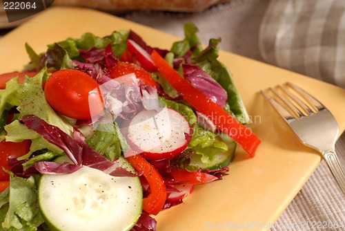Image of A crisp healthy salad with a fork on a yellow plate with rustic