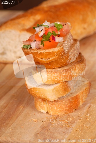 Image of Stack of bruschetta on a cutting board with loaf of bread in bac