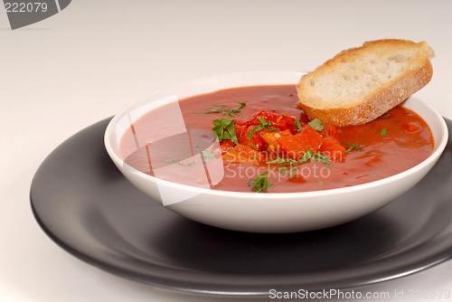 Image of Tomato, red pepper, basil soup in white bowl with bread on a lig