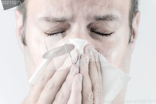 Image of Ill man with tissue is sneezing