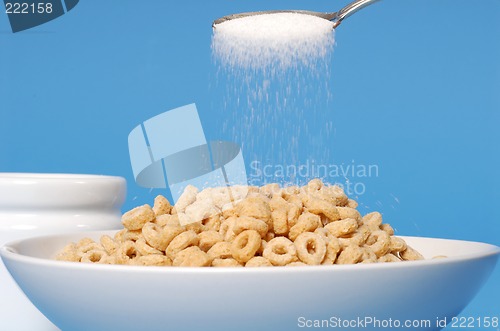 Image of Spoon sprinkling sugar on a bowl of oat cereal on blue backgroun