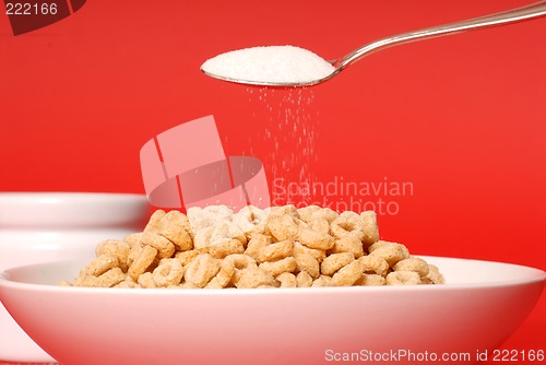 Image of A spoon sprinkling sugar on a bowl of oat cereal on red backgrou