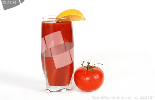 Image of Glass of tomato juice with lemon wedge and tomato next to glass