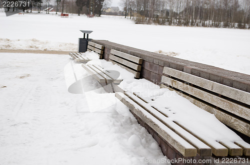 Image of wooden park bench waste bin cover snow in winter 