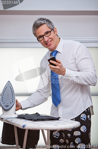 Image of Businessman text messaging while ironing pants