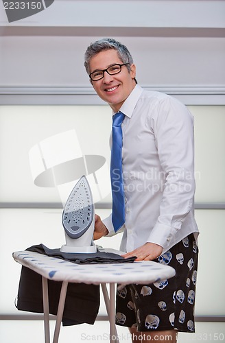 Image of Businessman smiling while ironing pants