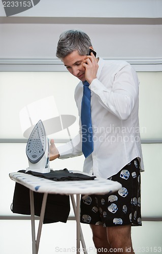 Image of Talking on a mobile phone while ironing pants