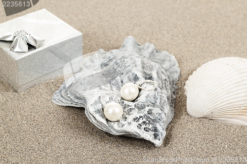 Image of two pearl earrings and shells on sand