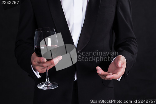 Image of Fragment of stylish man in elegant black tuxedo with glass red w