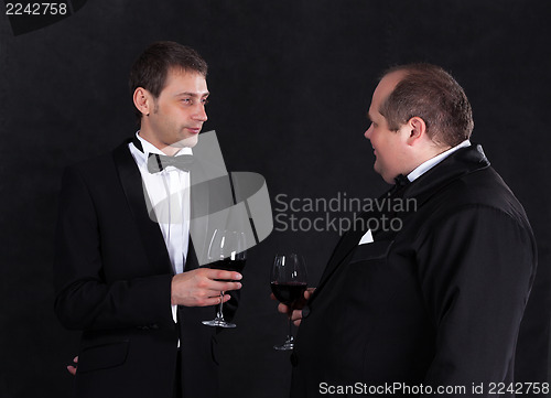 Image of Two stylish businessman in tuxedos with glasses of red wine
