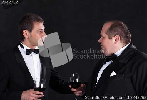 Image of Two stylish businessman in tuxedos with glasses of red wine